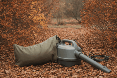 corded leaf vacuum with a collection bag lying on a thick layer of shredded leaves between shrubs in a planting bed