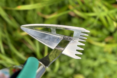 A garden hoe head held against foliage, the wide blade face and the row of tines both in view. The 5 Best Garden Hoes for Weeding (2026)