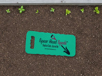 Spear Head Spade garden kneeler lying on dark soil beside a raised bed of seedlings
