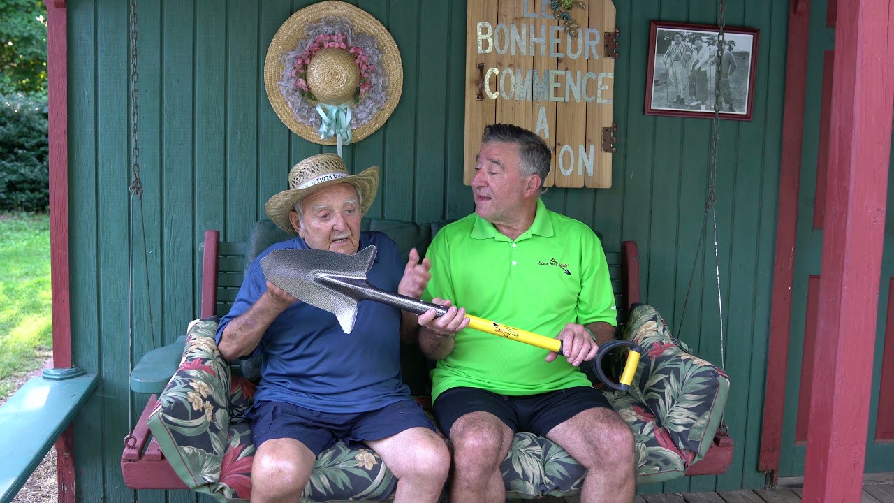 Daniel Mathieu in a straw hat and his son Julien in a green Spear Head Spade shirt, sitting on a porch swing holding the spade