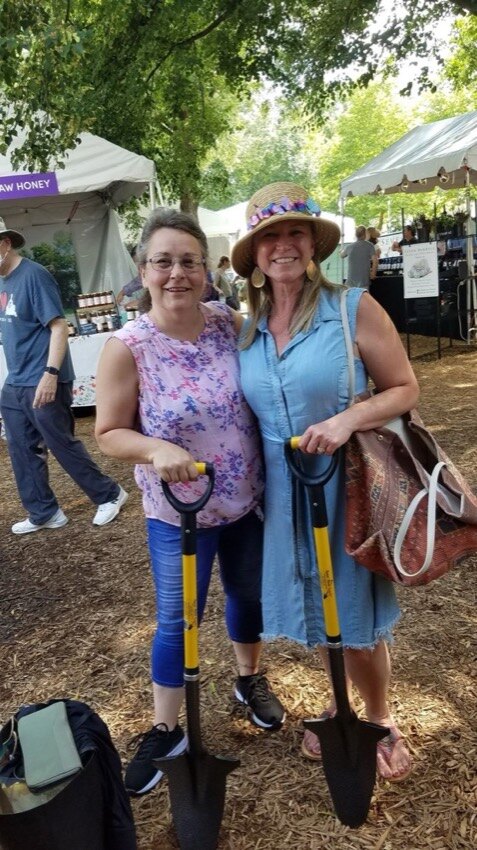 Two smiling women at an outdoor flower show holding D-handle Spear Head Spades