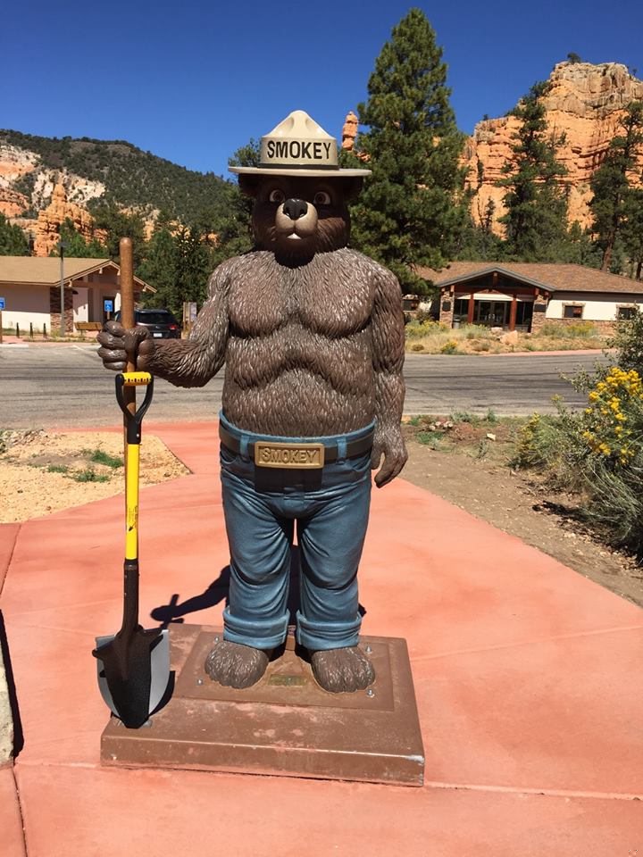 Smokey Bear statue holding a yellow Spear Head Spade in front of red rock hills