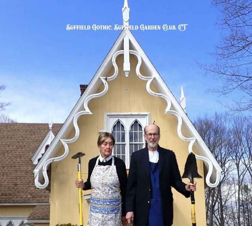 Two Suffield Garden Club members posing like the American Gothic painting with garden tools in front of a gothic style house