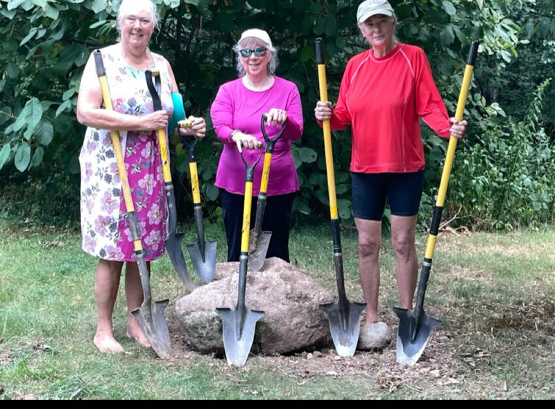 Three women standing in a garden holding Spear Head Spades around a large rock